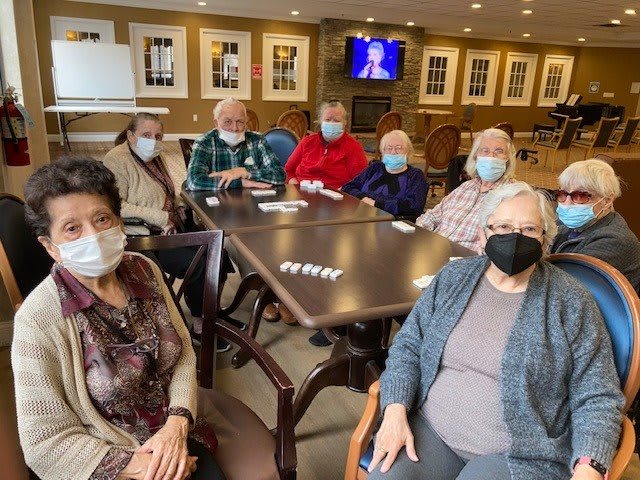 A group of seniors wearing masks gathered around a table indoors.