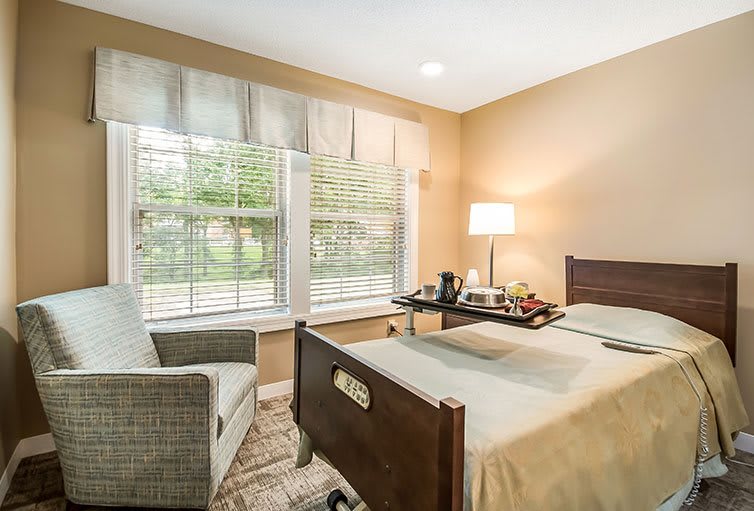 A cozy bedroom with a single bed, a comfortable chair, and a window letting in natural light.