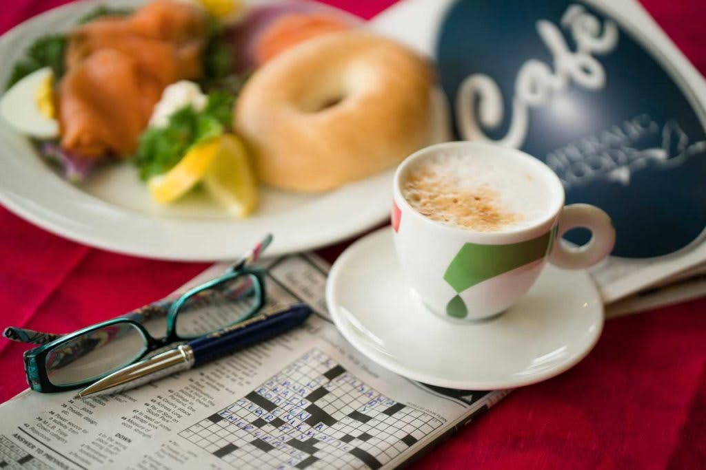 A cozy morning setup with coffee, a bagel breakfast, and a crossword puzzle.