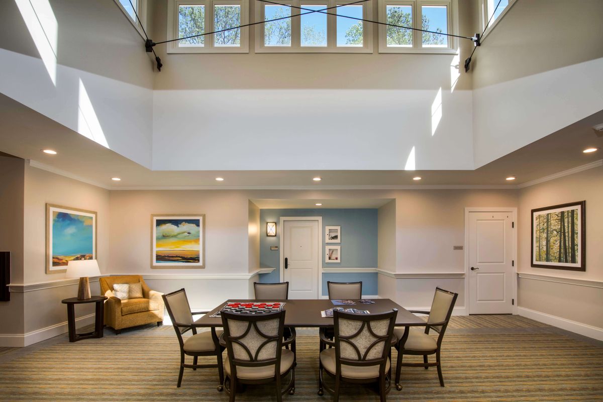 A modern living room with a central table surrounded by chairs under large windows.