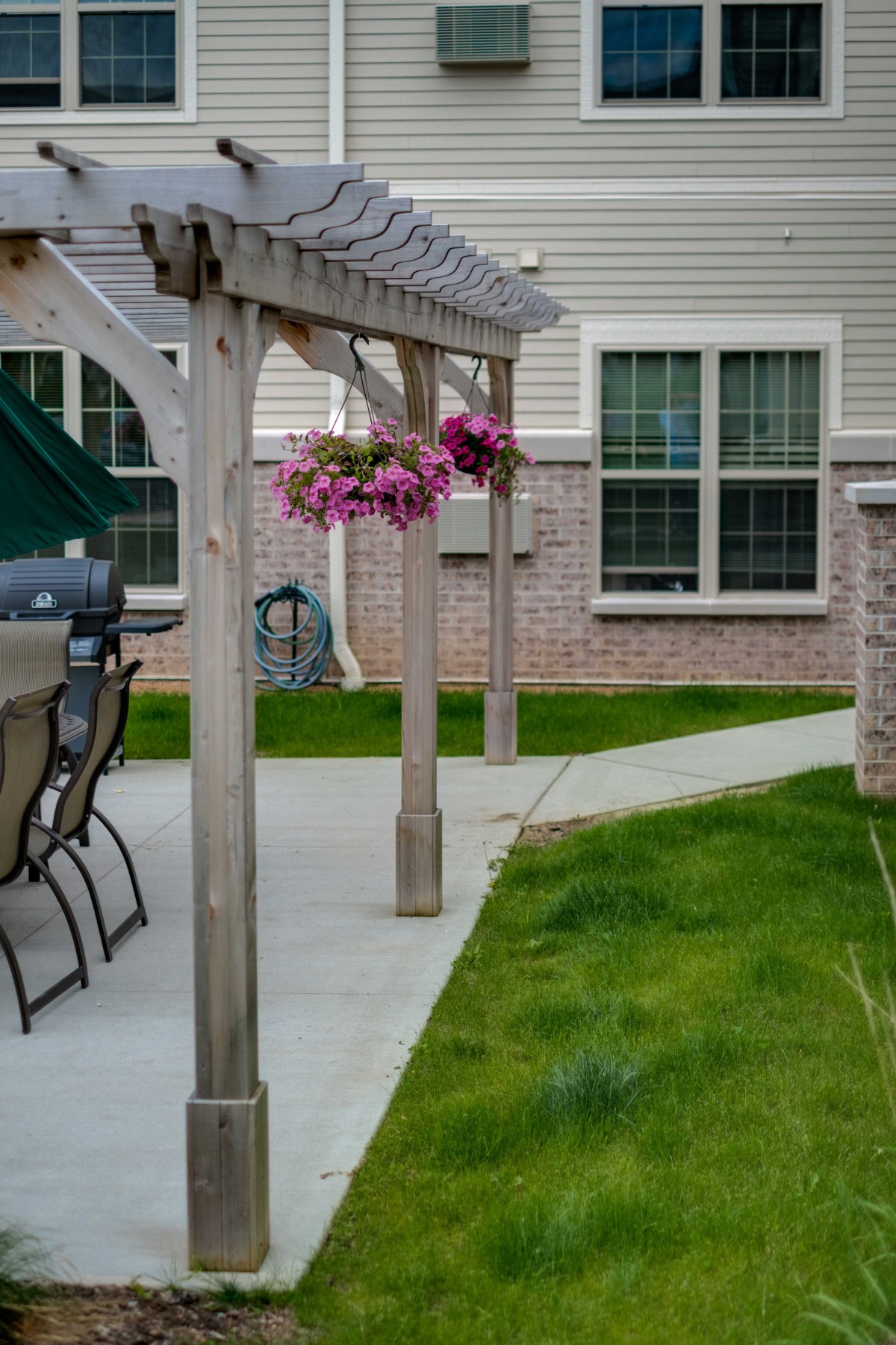 A backyard patio area with a pergola, hanging flowers, and outdoor seating.