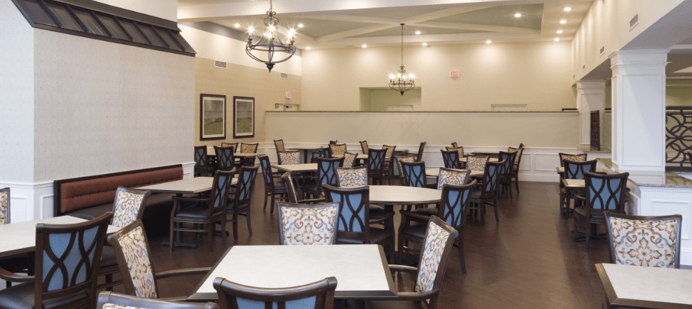 A spacious dining room with neatly arranged tables and chairs under elegant lighting.