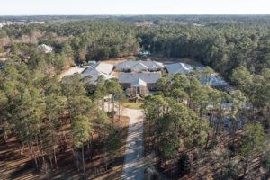 Aerial view of a large estate surrounded by a forest and featuring a long driveway.