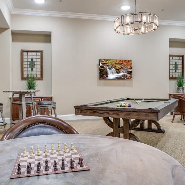 A modern game room featuring a chessboard and a billiards table, elegantly decorated with tasteful lighting and wall art.