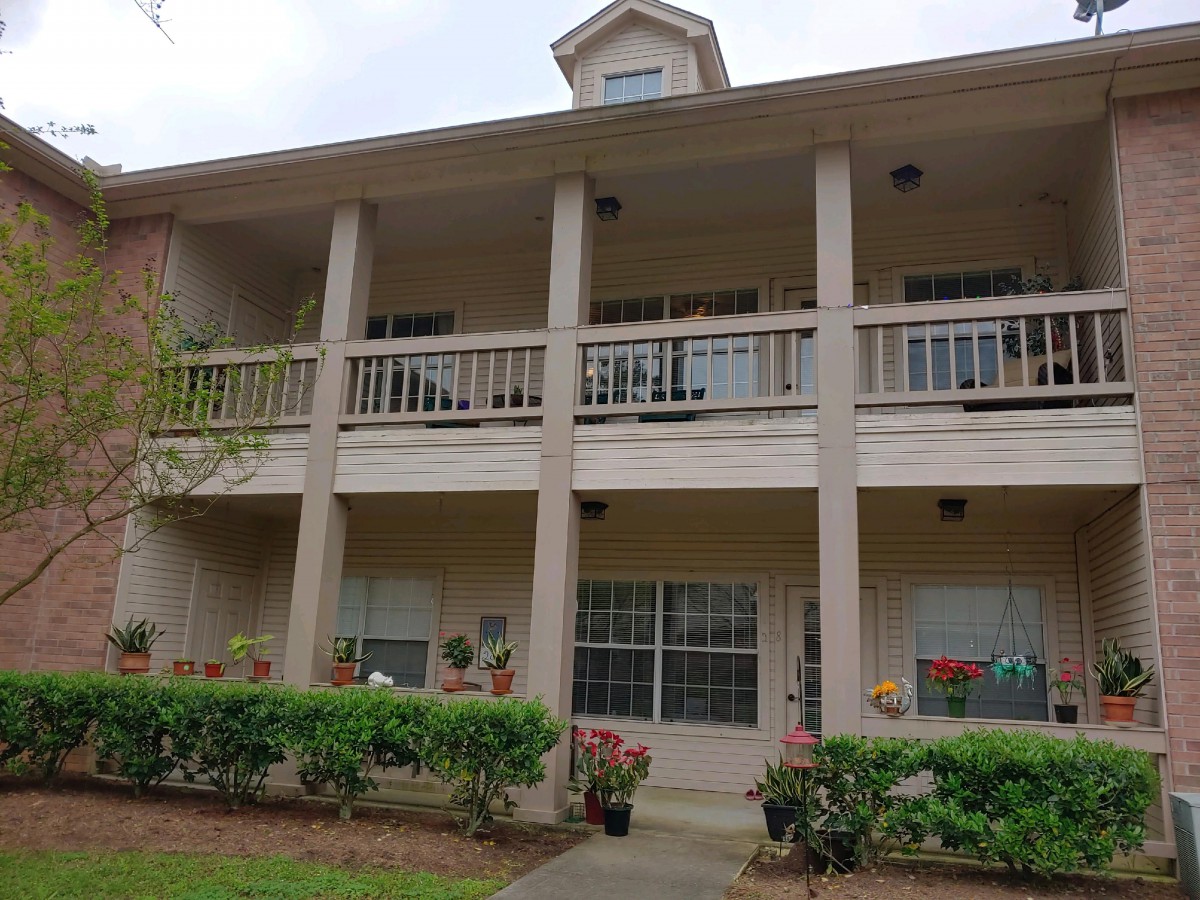 A two-story apartment building with balconies and landscaped surroundings.