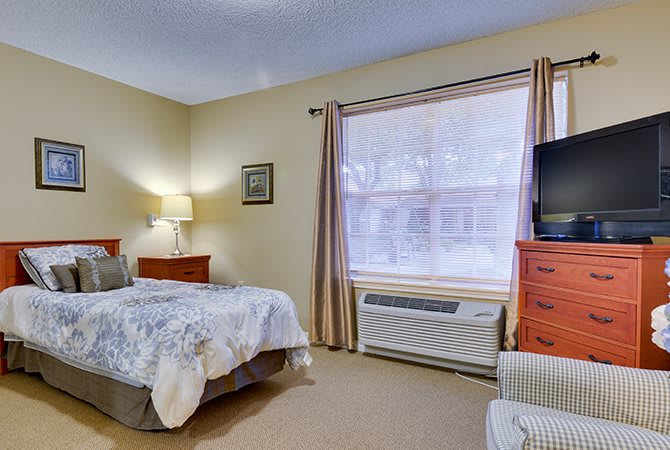 A cozy bedroom with a bed, TV, and large window.