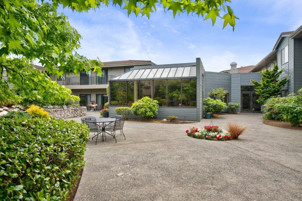 A spacious backyard patio featuring a sunroom and lush greenery.
