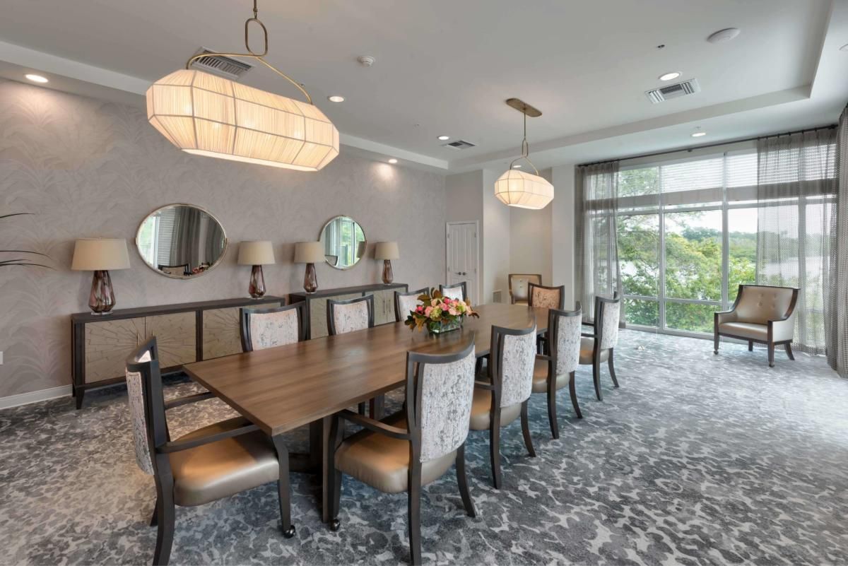 A modern dining room with a large conference table and elegant chairs, featuring pendant lighting and large windows for natural light.