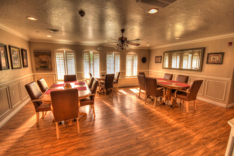 A warmly lit dining room with wooden floors, several tables, and chairs arranged around the room.