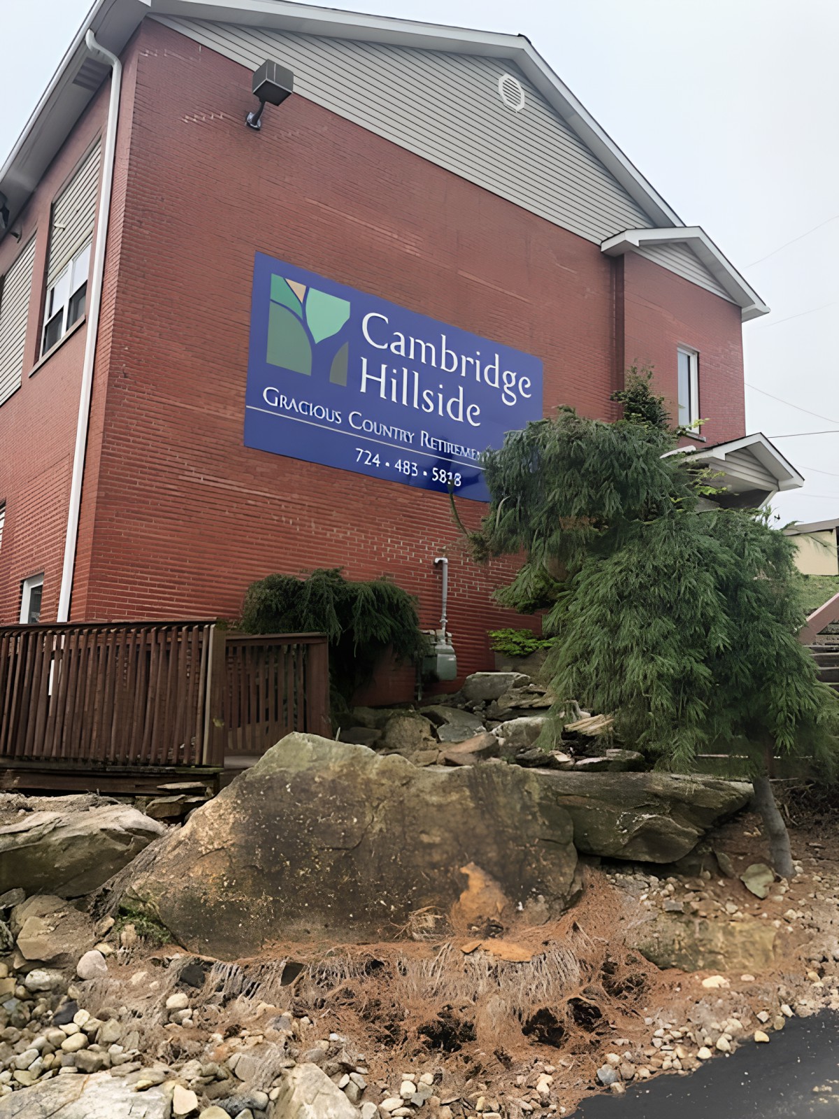 A brick building with a sign reading 'Cambridge Hillside' surrounded by rocks and greenery.