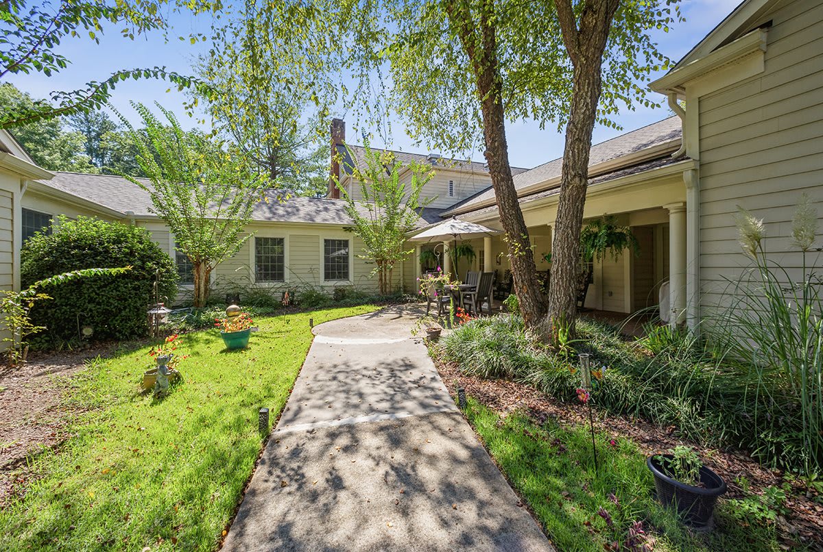 A beautiful home with a lush garden and trees lining the pathway.
