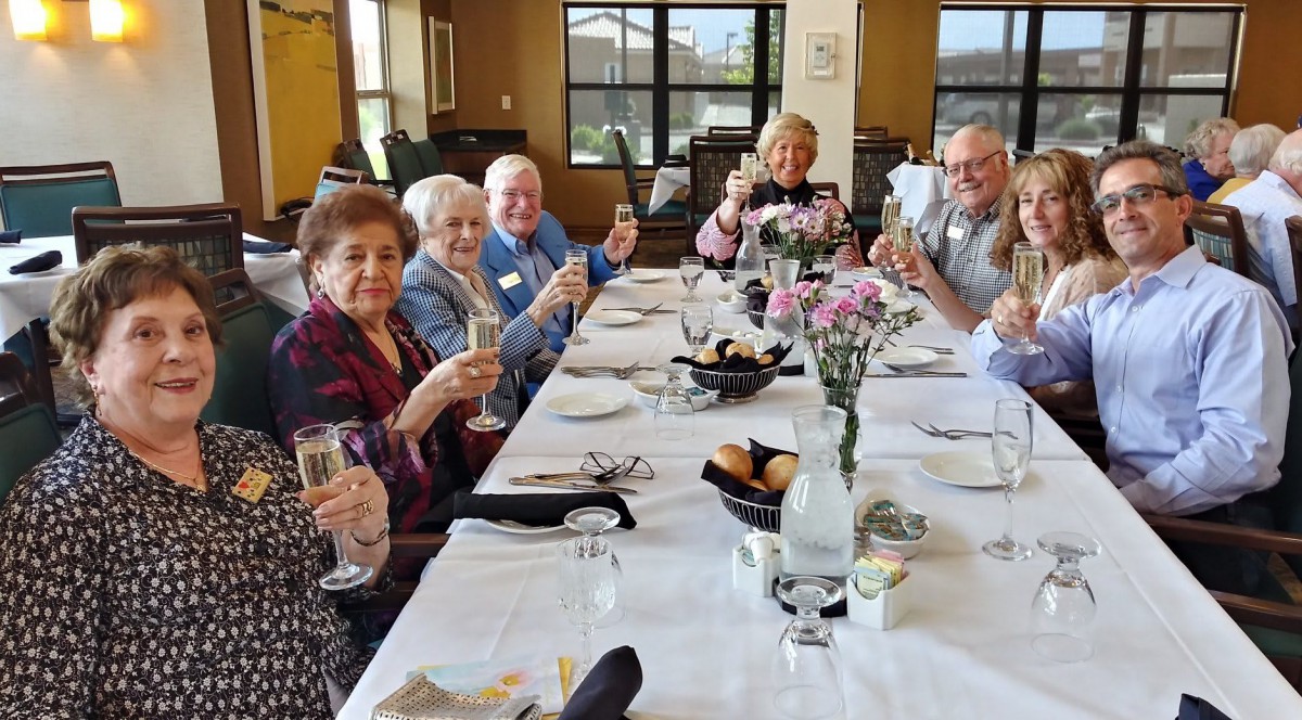 A group of elderly people enjoying a celebratory meal together, raising their glasses at a beautifully set dining table with floral decorations.