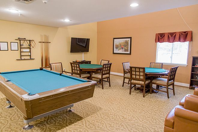 A cozy game room featuring a billiards table, multiple card tables with chairs, and a wall-mounted television.