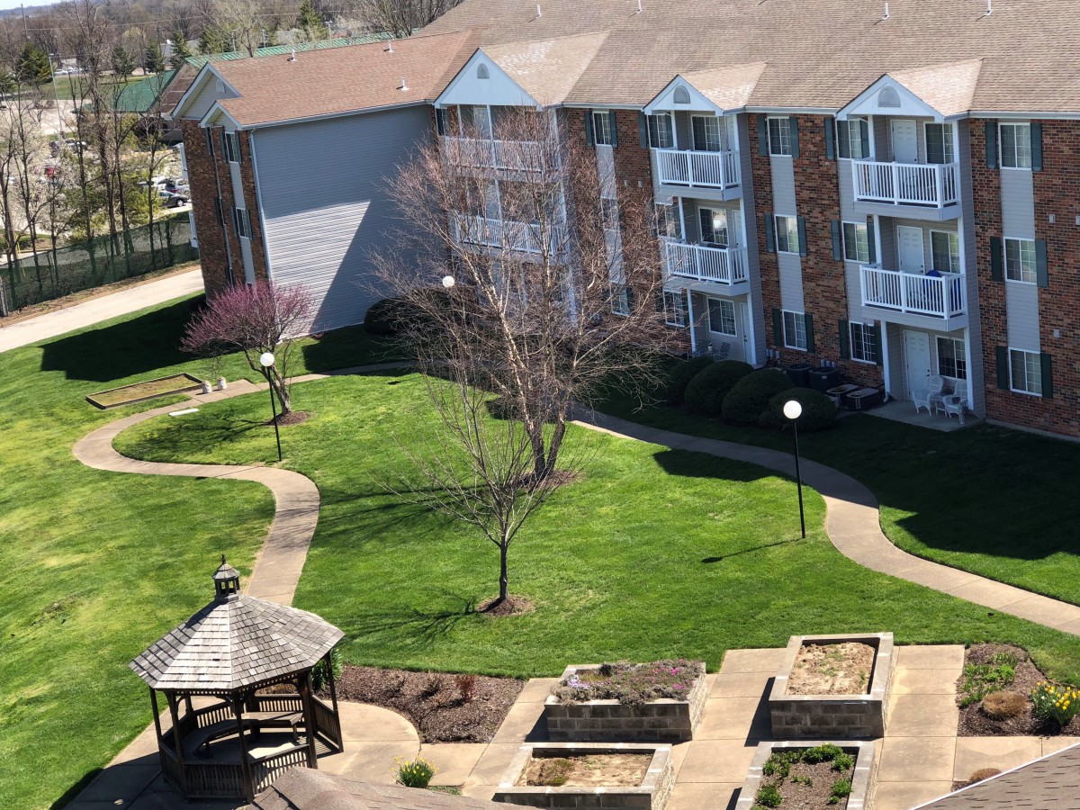 A view of an apartment building with a well-maintained courtyard featuring a gazebo and pathways.