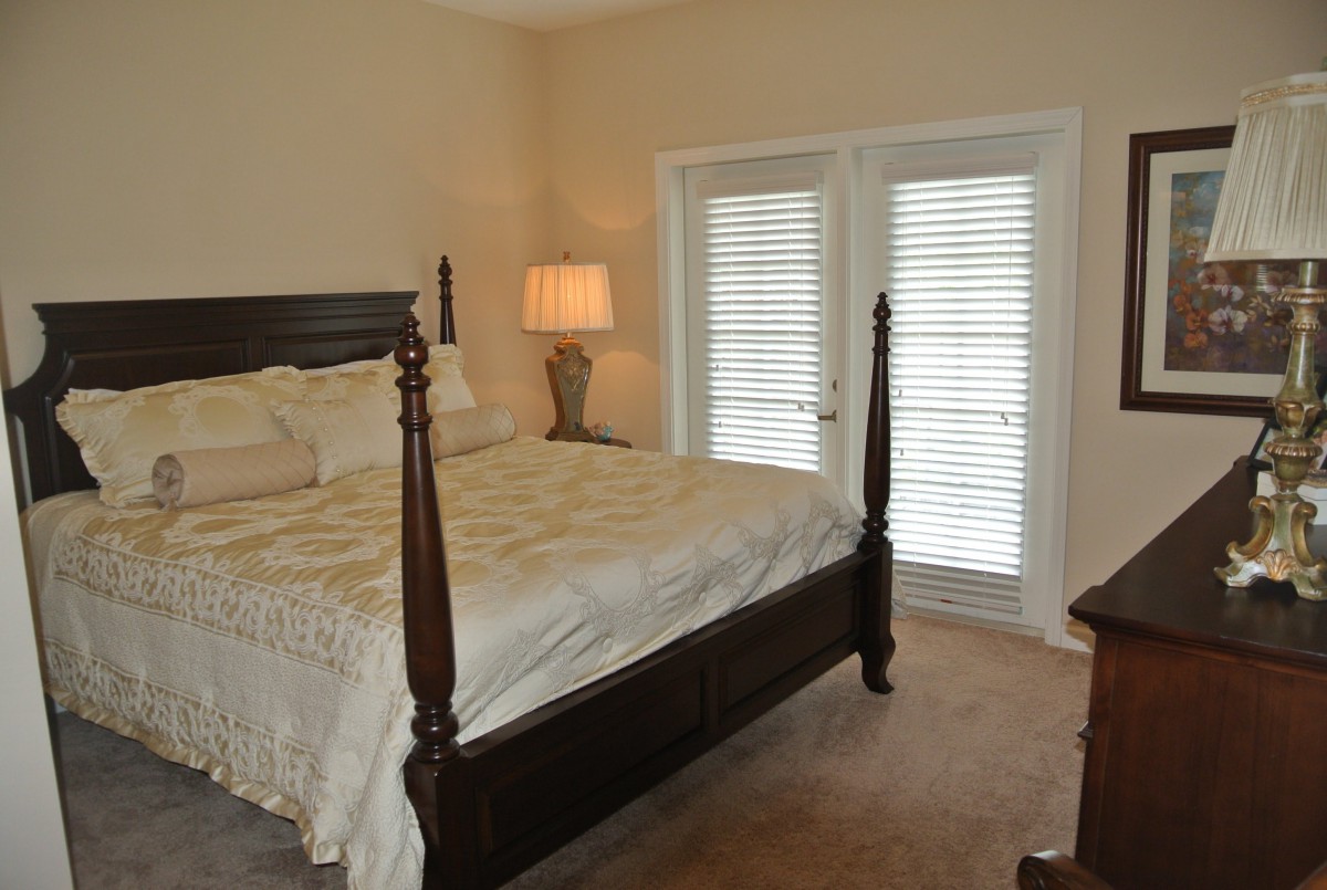 A cozy bedroom with a four-poster bed and a lamp near double doors.