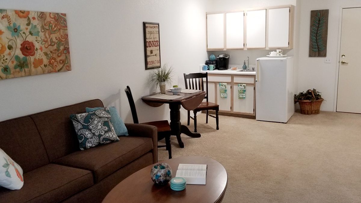 A cozy living area with a small kitchenette, featuring a sofa, table, and chairs.