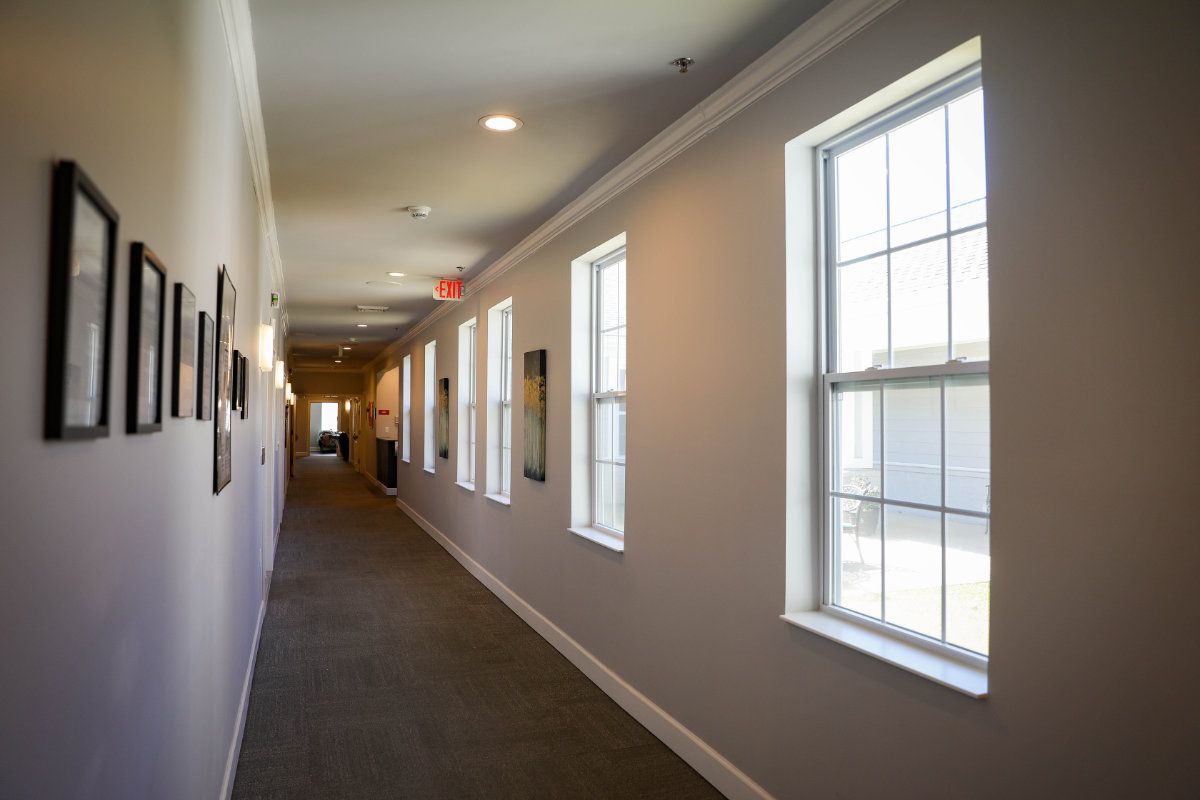 A well-lit indoor hallway with multiple windows and carpeted flooring.