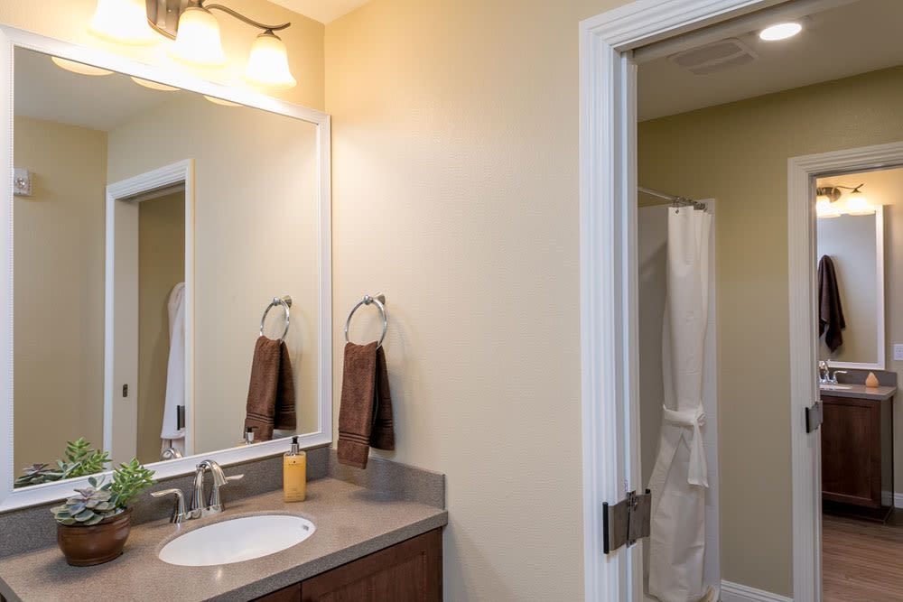 A clean bathroom featuring a sink with a mirror, towels on rings, and a view of a shower through an open doorway.