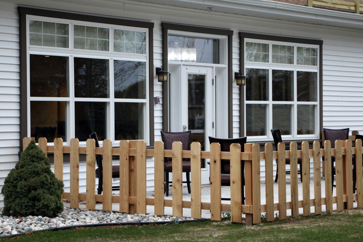 A cozy patio area of a house with large windows and a wooden fence.
