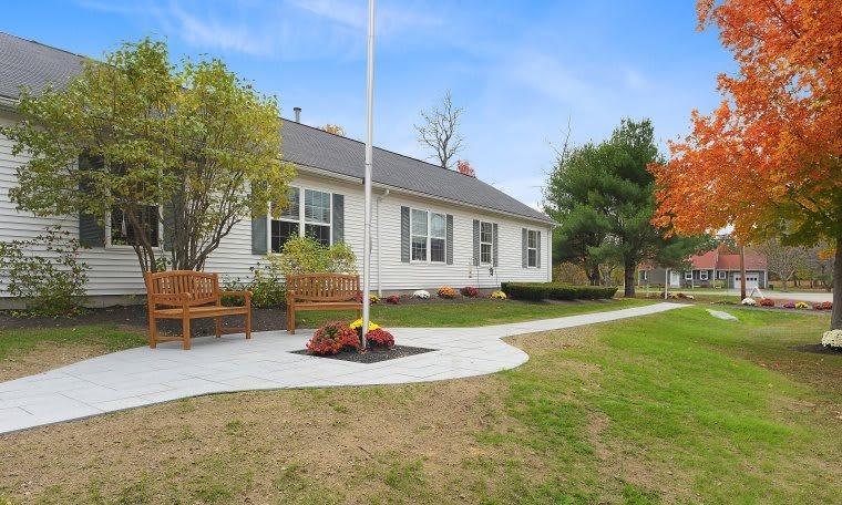 A suburban house with a well-maintained lawn and benches along a curved pathway.