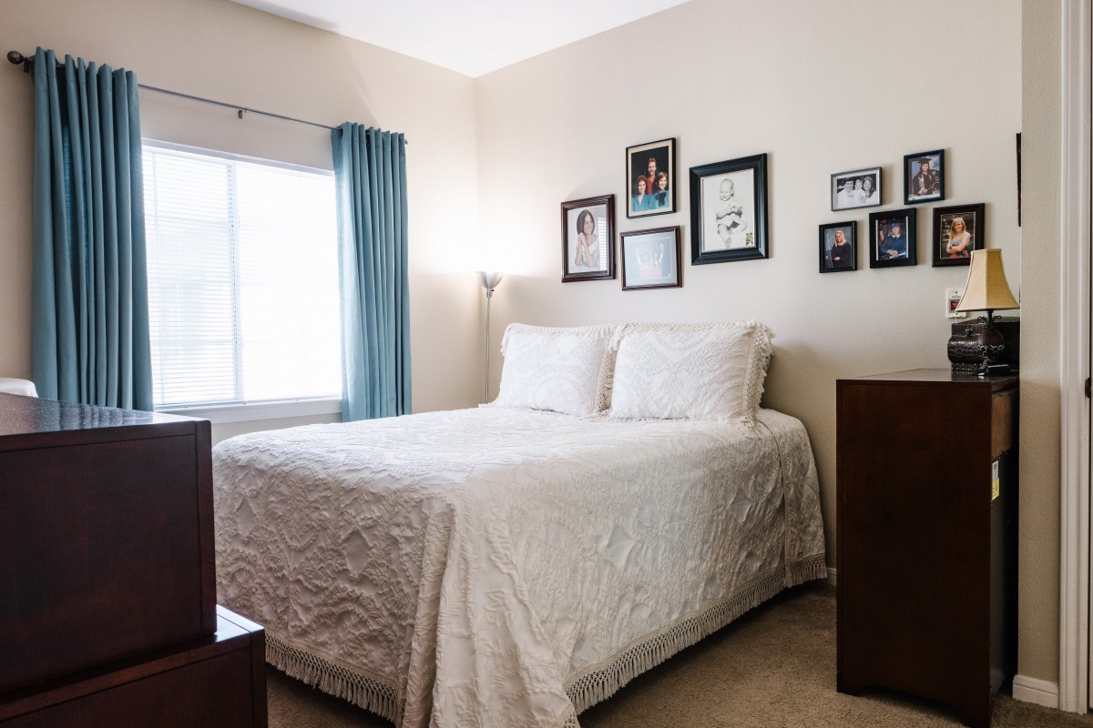 A cozy bedroom with framed artwork above the bed and light streaming through a window with blue curtains.