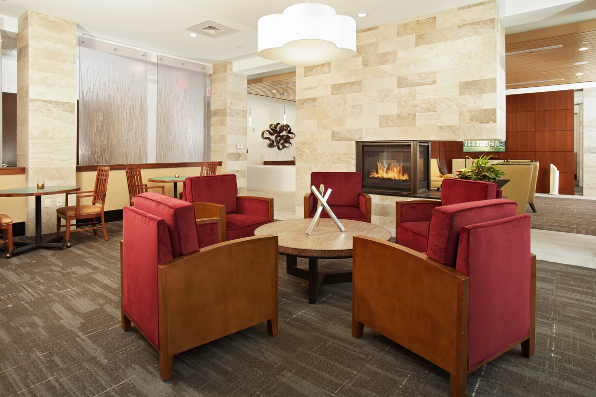 A modern lobby with red chairs arranged around a fireplace.