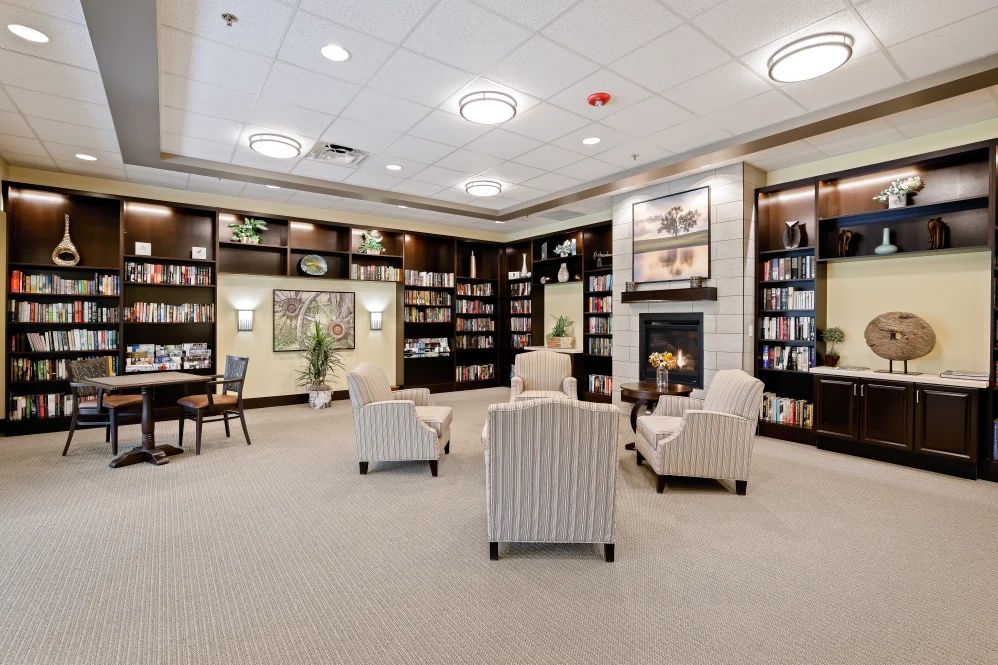 A cozy library setting with comfortable chairs and a fireplace, surrounded by bookshelves.