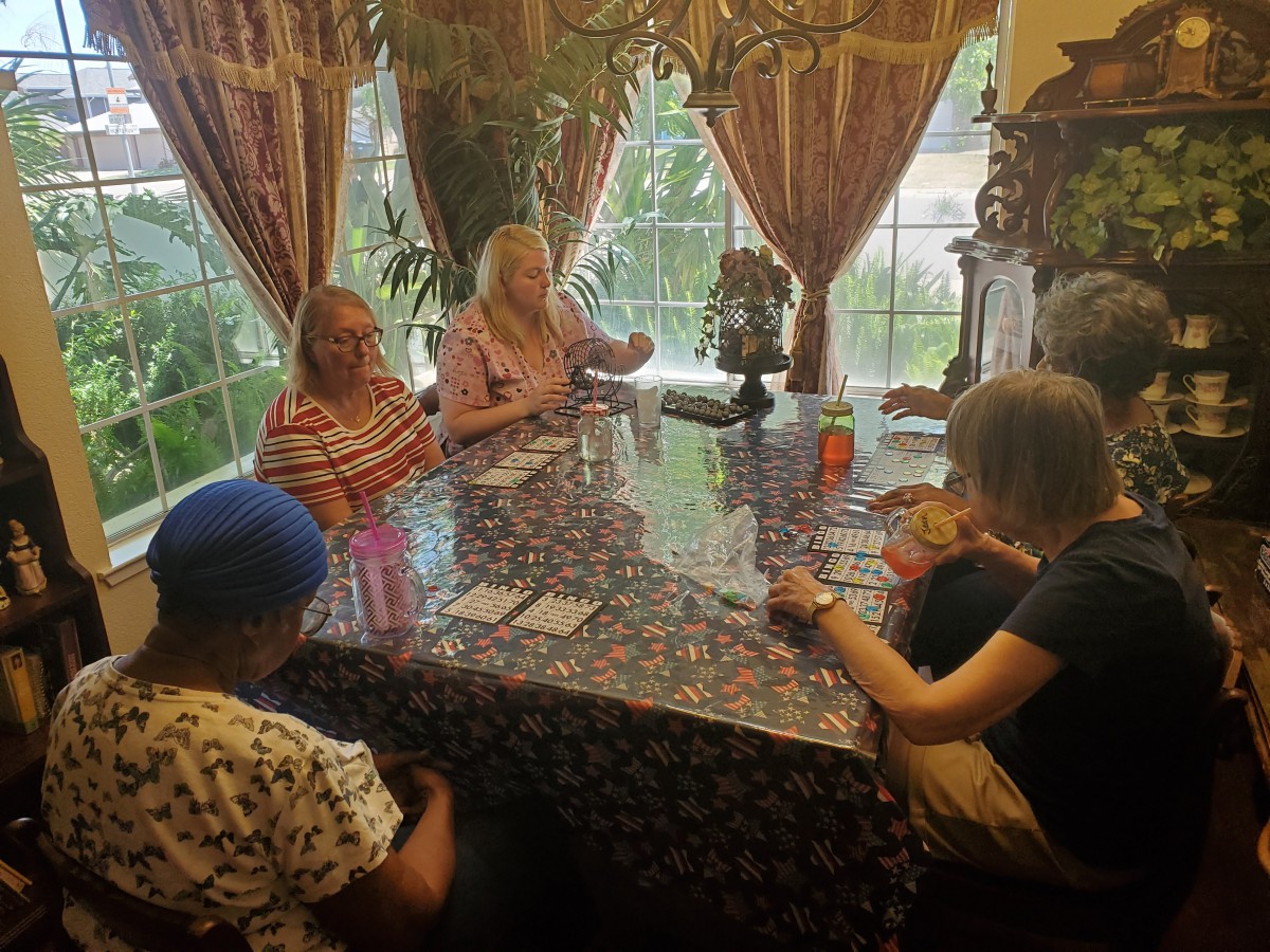 A group of people sitting around a table playing cards near a window with curtains.