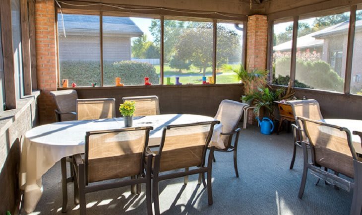 A sunny screened porch with a dining table and chairs, decorated with plants.