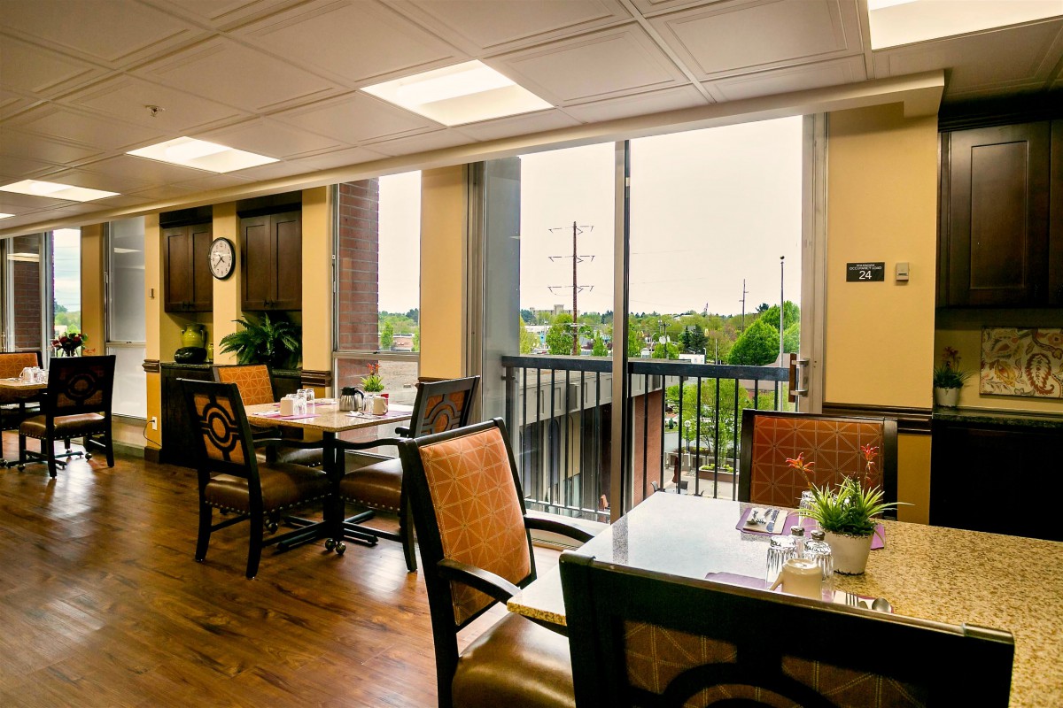 A well-lit dining area featuring several tables and chairs with large windows providing natural light.