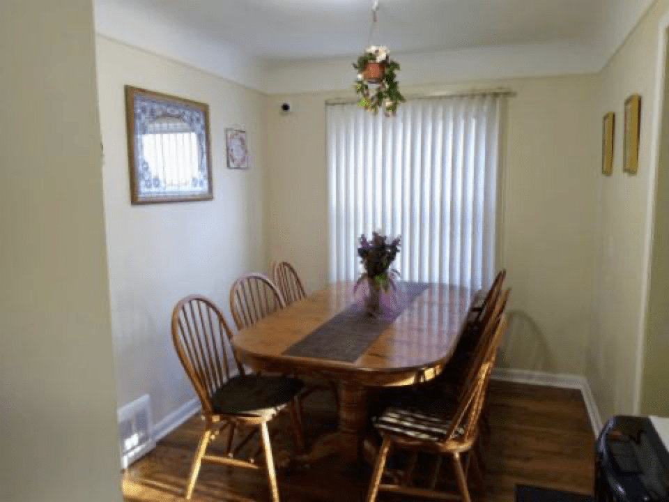 A cozy dining room with a wooden table and chairs, adorned with a flower arrangement and decorated walls.