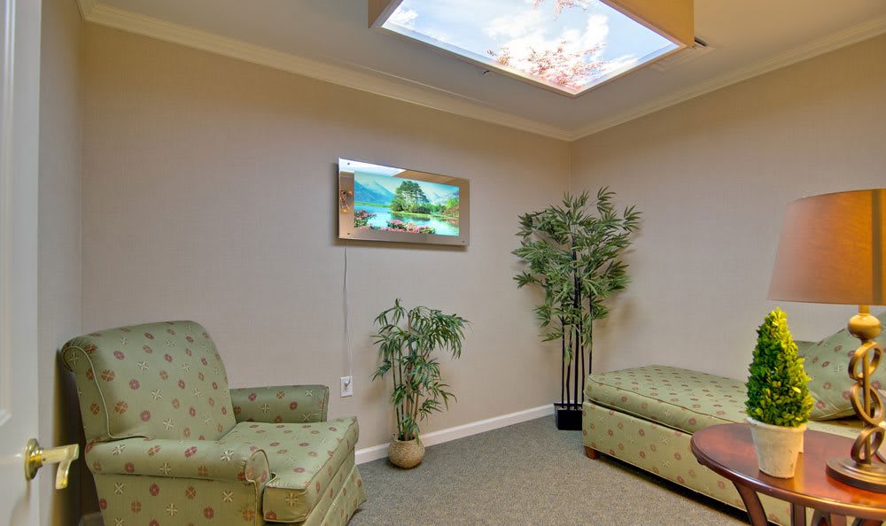 A cozy waiting room with comfortable seating, decorative plants, and a faux sky skylight.