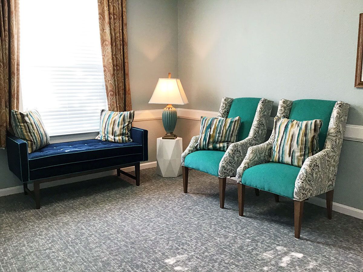 A cozy living room with teal chairs, a bench, and a lamp beside a window.