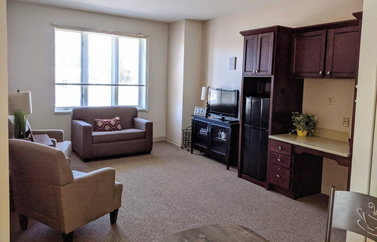 A cozy living room with armchairs, a television, and large windows.