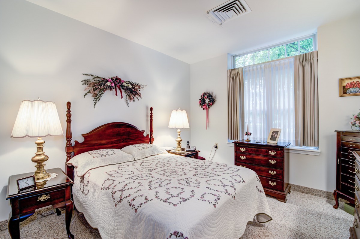 A cozy bedroom with traditional decor featuring a quilted bedspread, wooden furniture, and floral decorations.