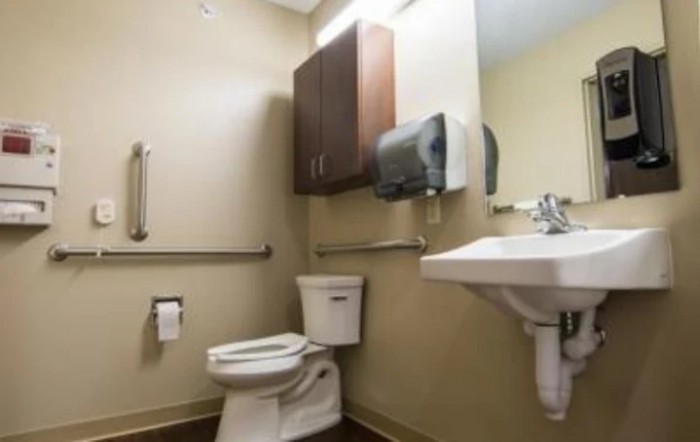 An accessible bathroom with a toilet, sink, and paper towel dispenser.