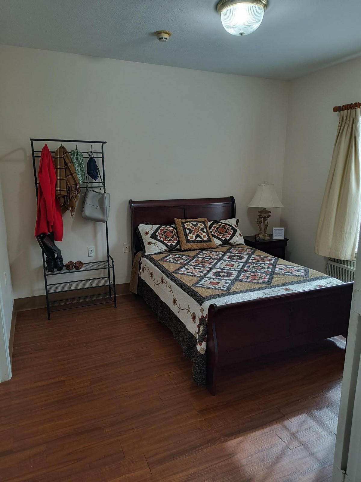 A cozy bedroom with a bed, clothing rack, and a lamp by the window.
