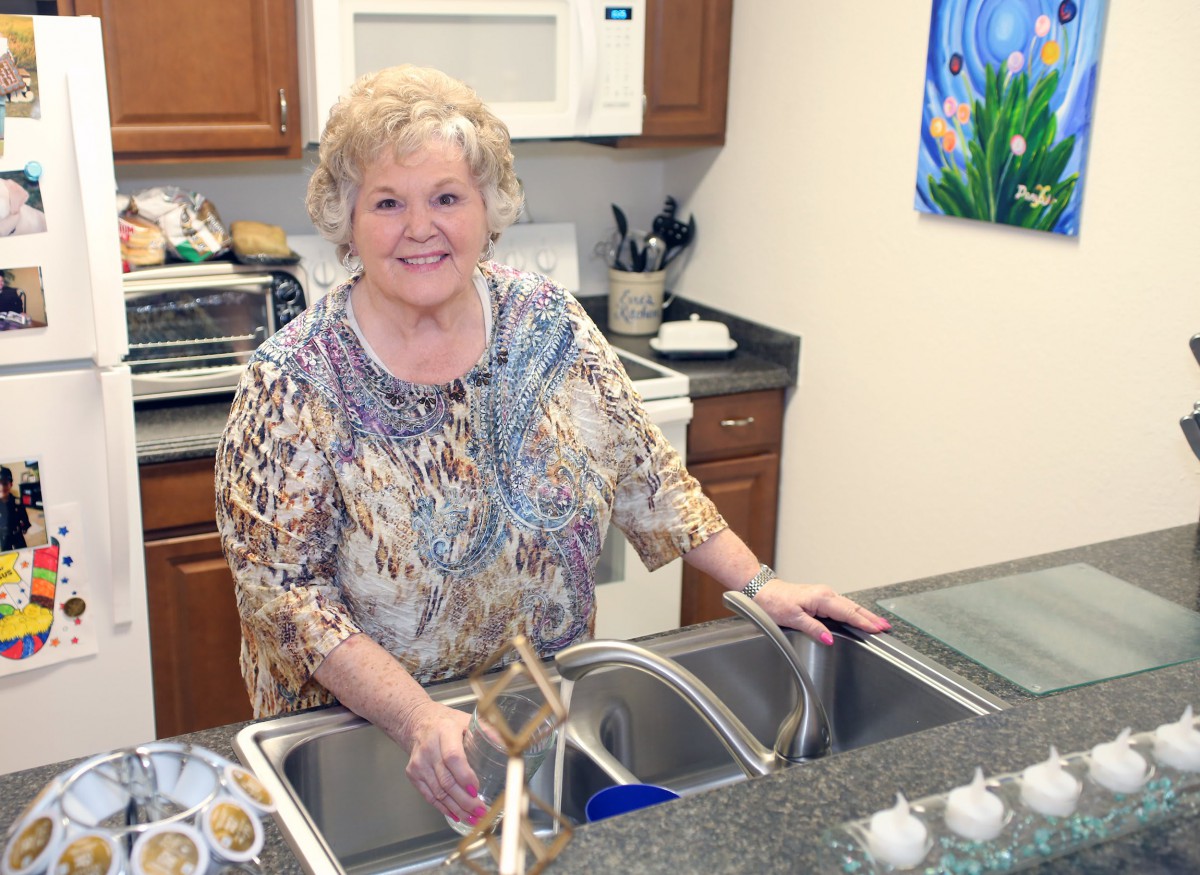 A woman standing in a kitchen near the sink, smiling.