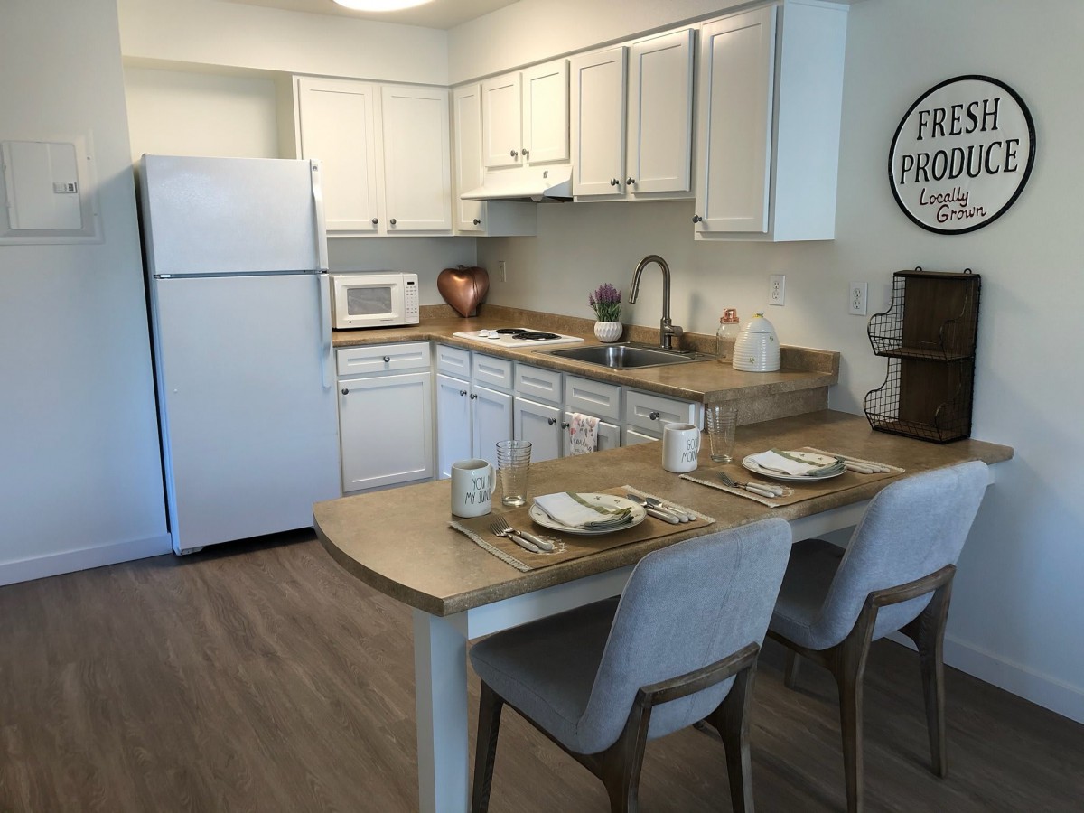 A modern kitchen with white cabinets, equipped with appliances and a small dining area with bar seating.