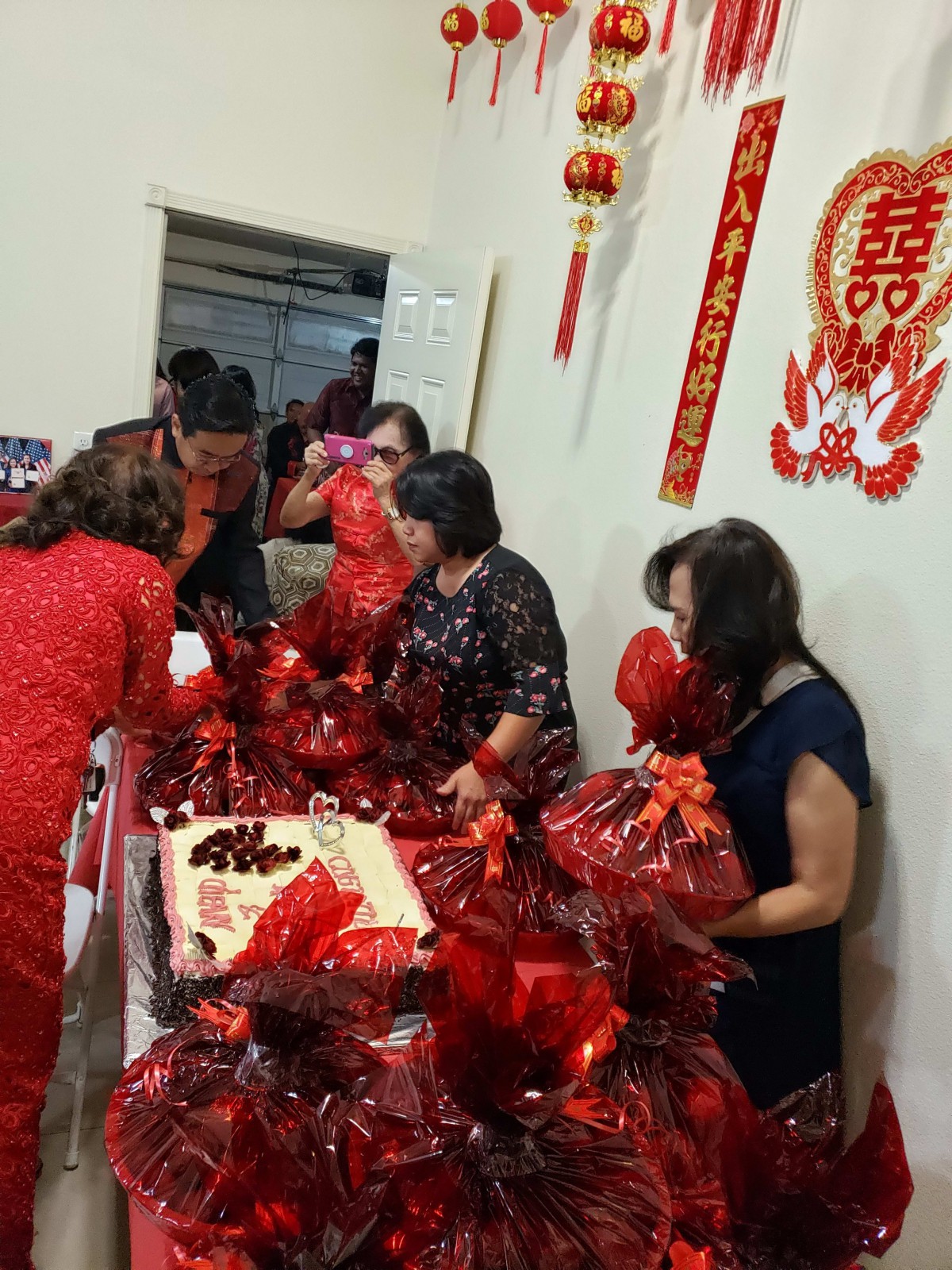 A group of people gather around a table with gifts wrapped in red, celebrating indoors.