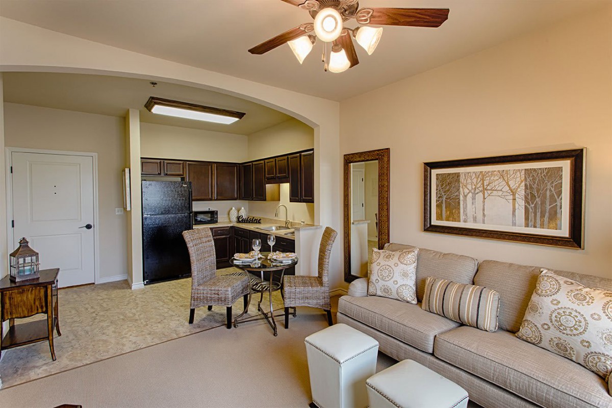 A cozy open-plan living and kitchen area in an apartment with a ceiling fan, sofa, and dining set.