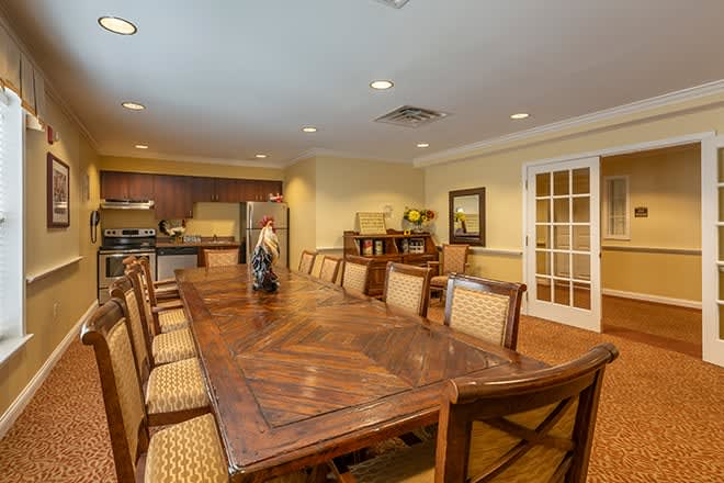 A spacious dining room with a large wooden table and chairs, adjacent to a kitchen area.