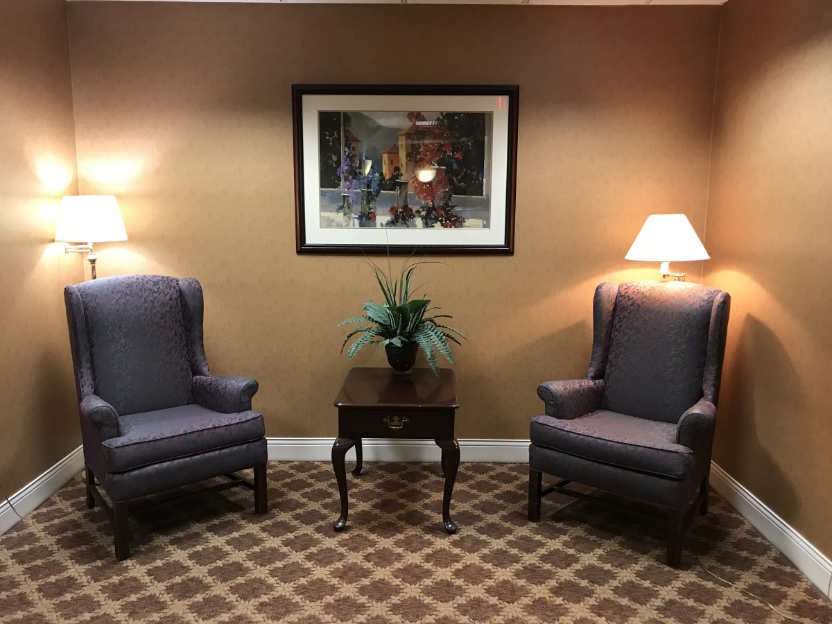 A cozy waiting room with two armchairs, a small table, lamps, and artwork on the wall.