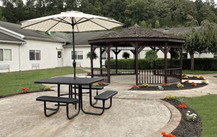 A peaceful outdoor patio area with a gazebo, picnic table, and umbrella in a garden setting.
