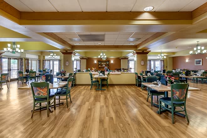A spacious dining room with wooden floors, neatly arranged tables and chairs, and elegant lighting fixtures.