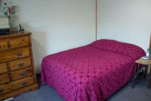 A bedroom with a bed covered in a pink quilt and a wooden dresser.