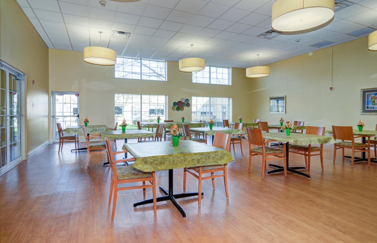 A spacious dining hall with multiple tables and chairs, featuring large windows and modern lighting fixtures.