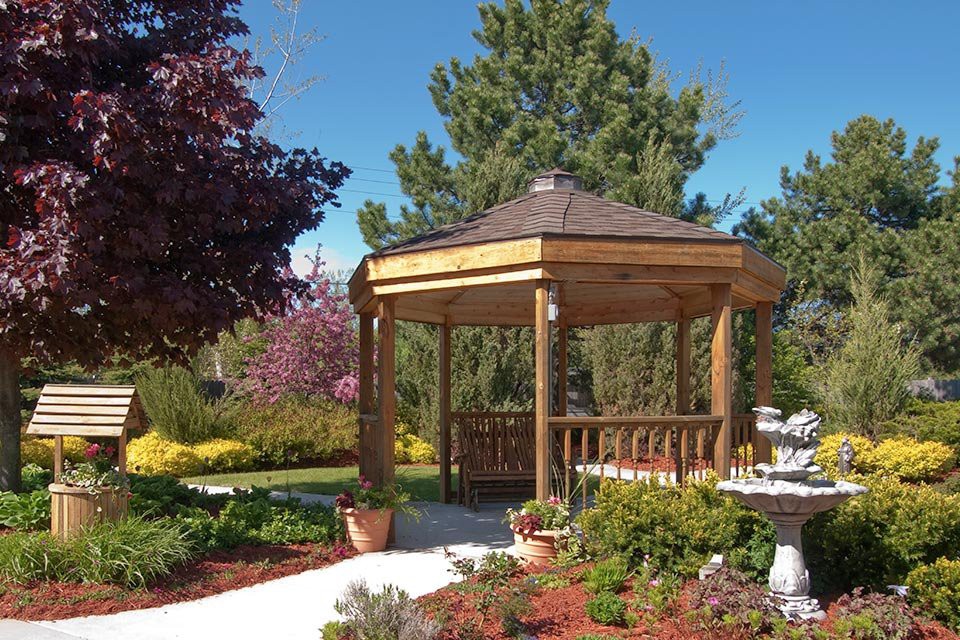 A wooden gazebo in a beautifully landscaped garden with colorful trees and flowers.