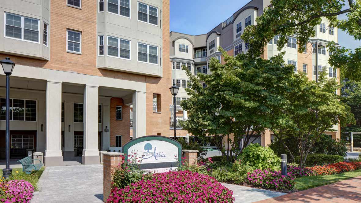 Entrance of a modern apartment building surrounded by landscaped gardens and vibrant flowers.
