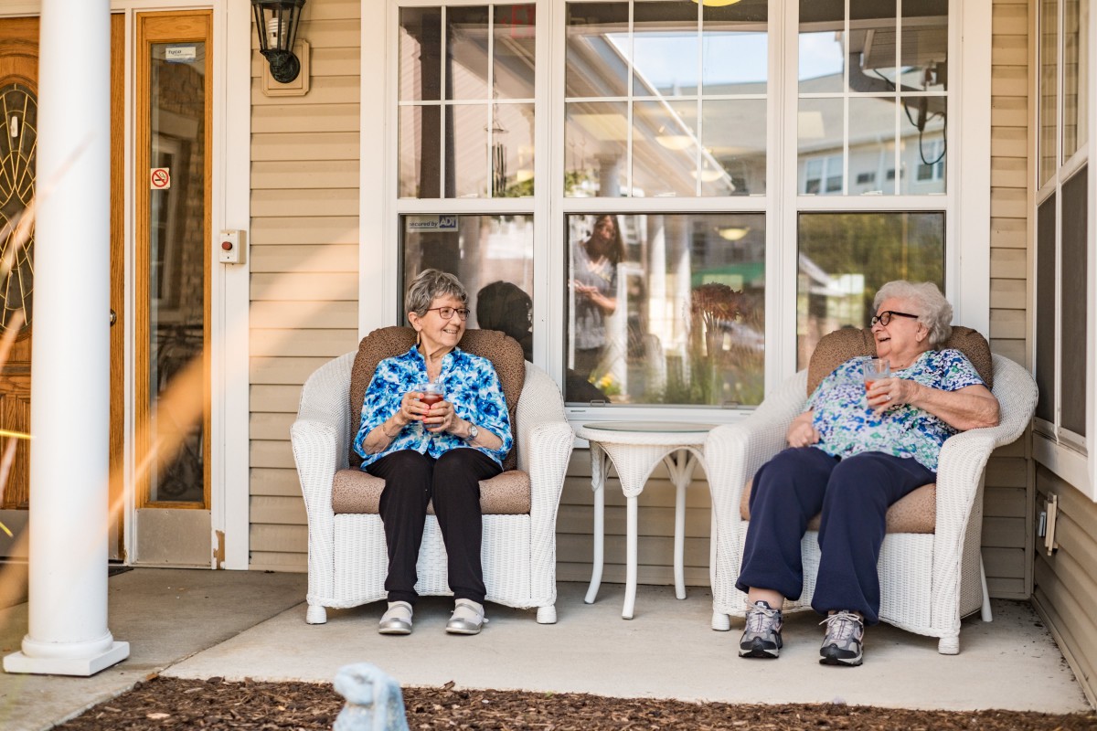 Two elderly individuals sitting and relaxing on a porch during the day.